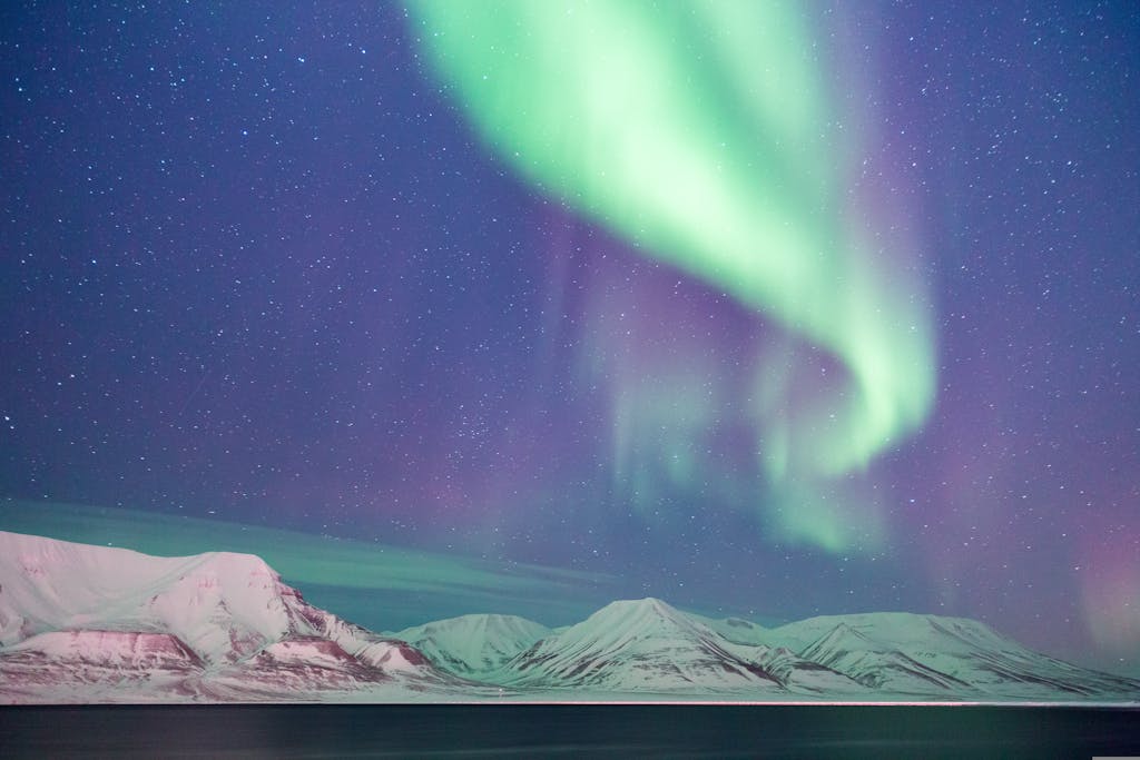 Stunning aurora borealis lights up the night sky over snowy arctic mountains.